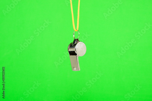 Foto A metal whistle with bright yellow lanyard hanging isolated against green backgr