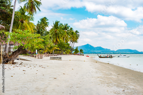 Koh Mook island, Kantang, Trang, Thailand, presenting a peaceful tropical beach with swaying palm trees, crystal clear water, and traditional longtail boats docked along the sandy shore