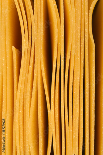 Macro view of multiple dried yellow lasagna pasta sheets stacked vertically with organic wavy lines and textured surfaces