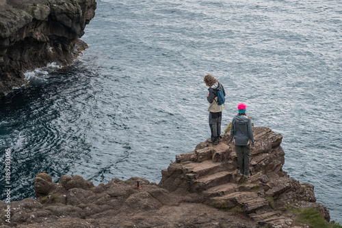 Young couple exploring gorge at seaside in village Gjogv, Faroe Islands