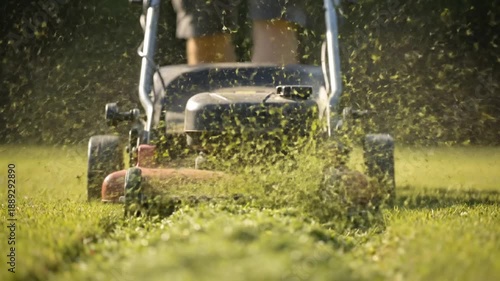 Close-up shot of a lawnmower cutting grass, green clippings fly in slow motion