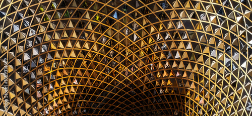 a modern architectural structure with a complex, curved design made of gold-tone metal and mirrored triangles