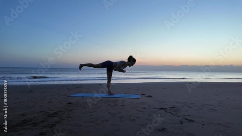 Lesbian woman practicing yoga balance pose on beach at sunrise