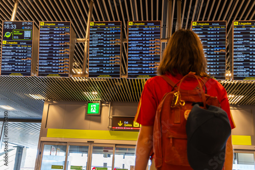 Schilderij op canvas Young woman with backpack and cap on her back looks at the flight boards at the