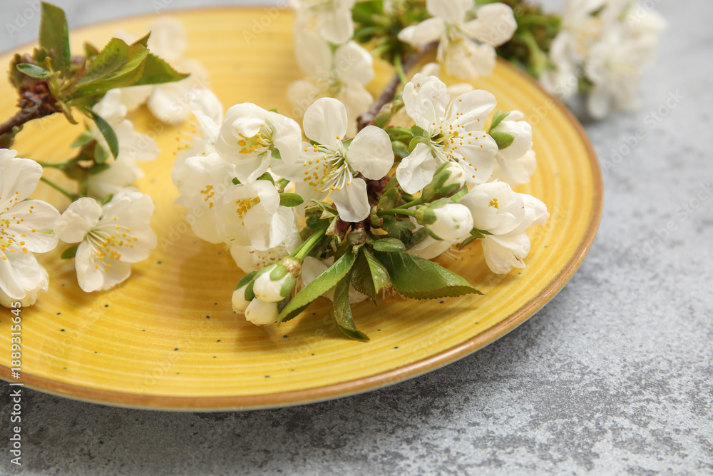 Naklejka premium Clean yellow plate with blooming branches on grey background, closeup