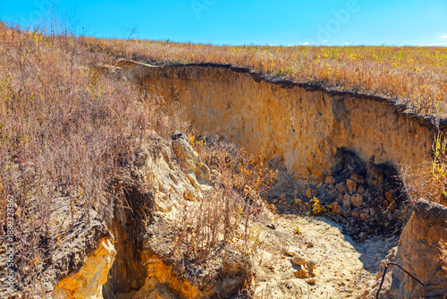 Deep gully cuts through eroded land, exposing layered soil with sparse vegetation clinging to surface. Degradation and the vulnerability of barren terrain to environmental forces