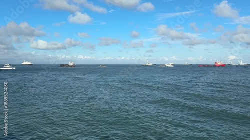 Several cargo ships and ferries anchored in Panama Bay, with shipping traffic on a sunny day against a cloudy backdrop