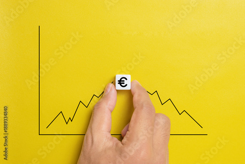 Predicting the market fluctuation in euro currency. Hand holds the dice with euro symbol with an increasing and declining graph.