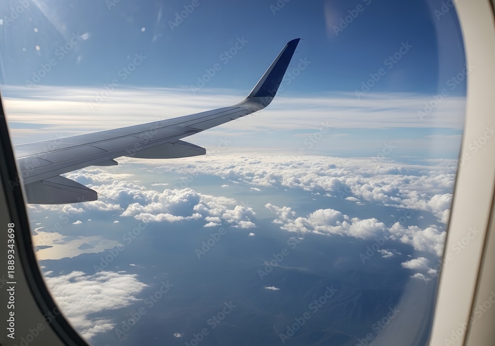 Obraz premium Airplane Wing View from Window Flying Above Clouds with Blue Sky and Sunlight During Travel Journey