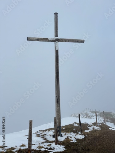 Large wooden cross stands alone on snowy hill under foggy sky in mountain area during winter season