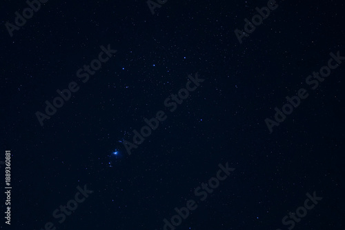 A deep view of the night sky featuring the bright stars of the Orion constellation and the faint blue glow of a nebula against deep black