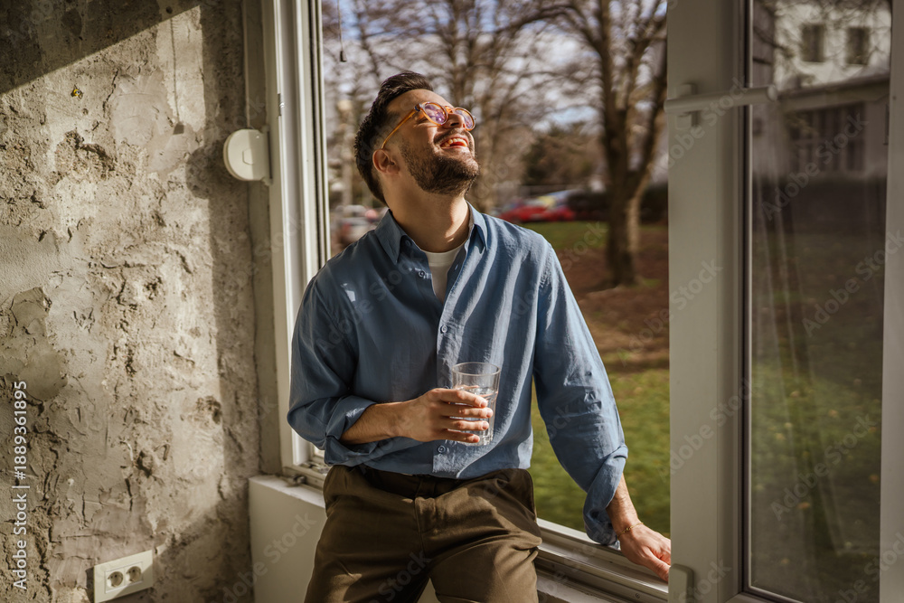 Obraz premium Young man enjoying morning sunlight by window with water
