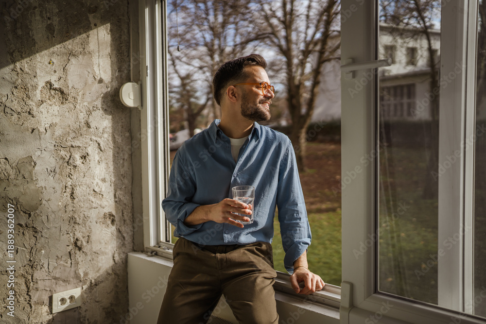 Fototapeta premium Happy man in casual wear drinking water at window