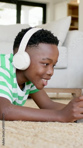 Vertical video: Smiling kid in green T reaching tablet appearing on home rug, watching with headset
