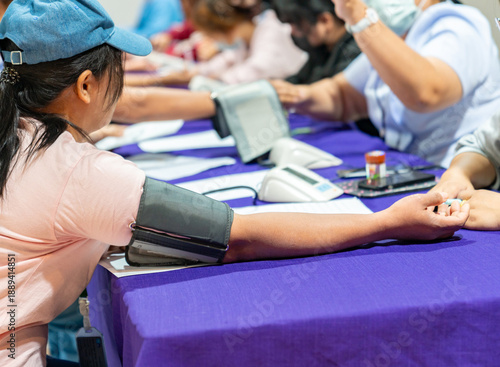 A row of people sitting at a long table undergoing blood pressure screenings.