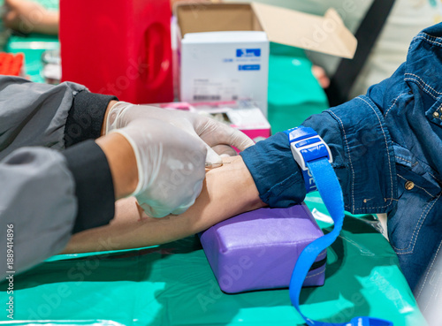 The patient is wearing a denim jacket, and a blue plastic tourniquet is secured around their upper arm.