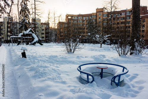 Wallpaper Mural Empty snowy playground with buried merry-go-round and slide amidst bare trees and apartment buildings, suggesting a quiet winter day Torontodigital.ca