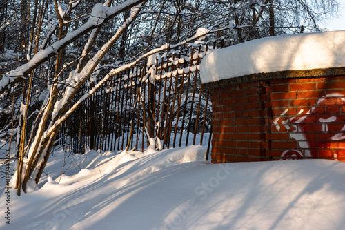 Wallpaper Mural Winter scene featuring snow drifts, stark tree branches covered in white, and a sunlit brick pillar against a dark metal fence Torontodigital.ca