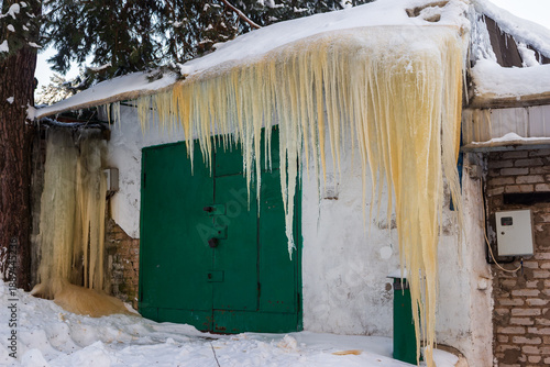 Wallpaper Mural Massive yellowish icicles hang from an old garage roof, transforming the weathered walls into a frozen winter spectacle. Nature's frosty grip creates a unique, chilly scene Torontodigital.ca