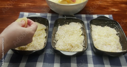 Chef sprinkles grated parmesan cheese over thinly sliced potatoes arranged in baking dishes. Close-up of food preparation, homemade potato casserole, rustic kitchen, natural light, traditional recipe