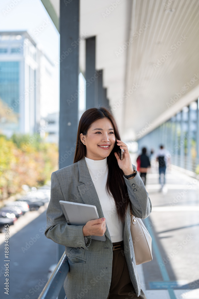 Fototapeta premium Asian woman student office worker talking on phone holding tablet as standing walking on footbridge.