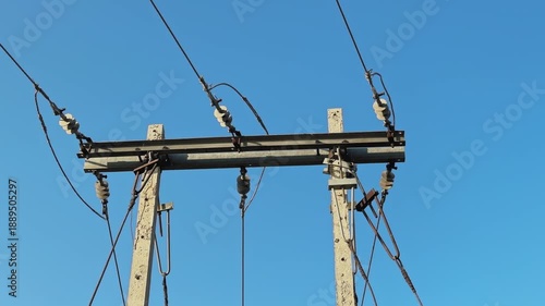 Static medium shot of a PSC or reinforced cement concrete power distribution pole in India, steel crossarm and ceramic insulators supporting low to medium voltage lines against a clear blue sky.