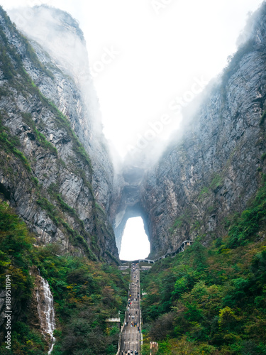 Foto Tianmen Mountain Heaven's Gate in Zhangjiajie, China, features a breathtaking natural rock arch with a long staircase surrounded by misty cliffs, attracting global adventure travelers