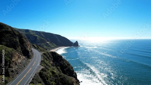 Aerial drone footage of winding coastal highway overlooking Pacific Ocean waves and cliffs