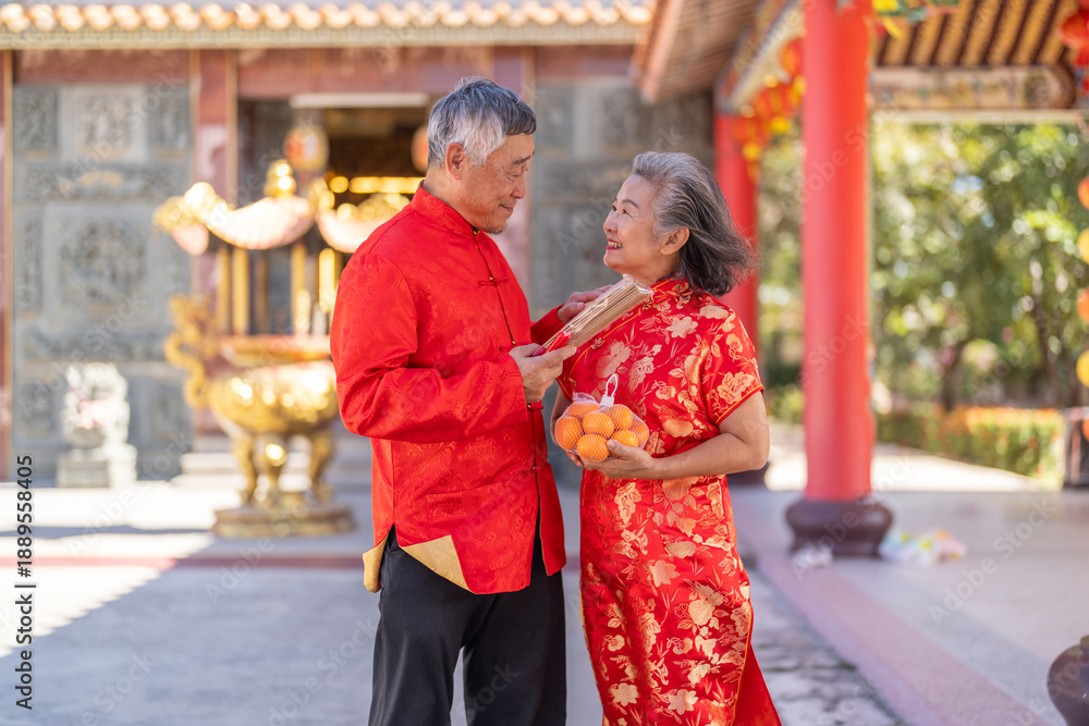 Naklejka premium Happy senior asian couple holding mandarin oranges and incense sticks at Chinese temple, Elderly husband and wife celebrating Lunar New Year, worship, traditional culture and retirement concept