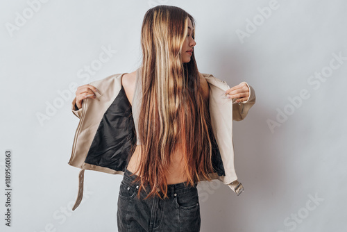 Εκτύπωση καμβά Young woman with long hair removing beige jacket and wearing sleeveless top standing against white background for fashion and style concept