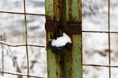 Wallpaper Mural An old, rusty padlock, dusted with fresh snow, secures a weathered green metal gate post in a bleak winter landscape. Decay and forgotten security Torontodigital.ca