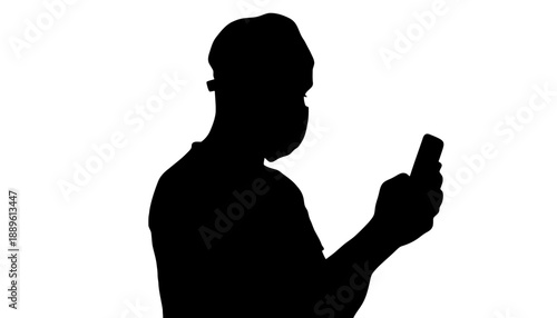 A silhouette of a man wearing a face mask and using his smartphone