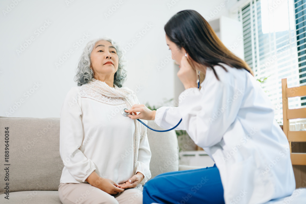 Obraz premium Healthcare professional using stethoscope to examine elderly woman at home. Senior medical checkup, heart health, home care, diagnosis, prevention
