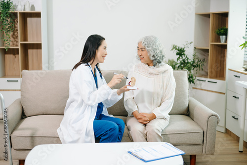 Female doctor explaining ear anatomy to elderly woman during home medical consultation. Hearing care, senior health, audiology, prevention, wellness and healthcare