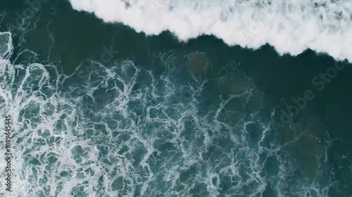 Top-down drone view of ocean waves crashing onto shoreline, water creating abstract paint-like patterns, slow motion, hypnotic movement, clean minimal composition, cinematic aerial footage