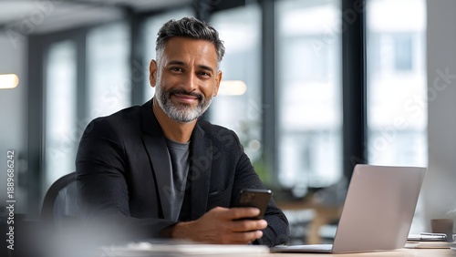 Smiling Middle Aged Businessman CEO Using Smartphone and Laptop in Modern Office