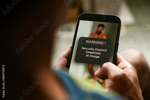 Man got warning message on mobile phone about viewing AI generated sexualized imagery in social media using Deepfake technology. Selective focus on the phone.