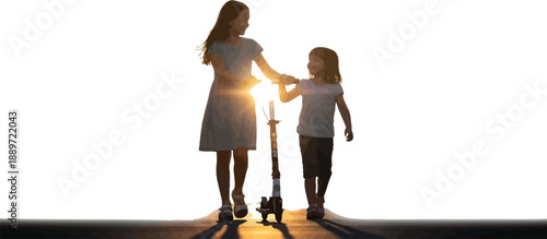 Two young sisters silhouette walking together down a path pushing a scooter against the bright setting sun flare outdoors