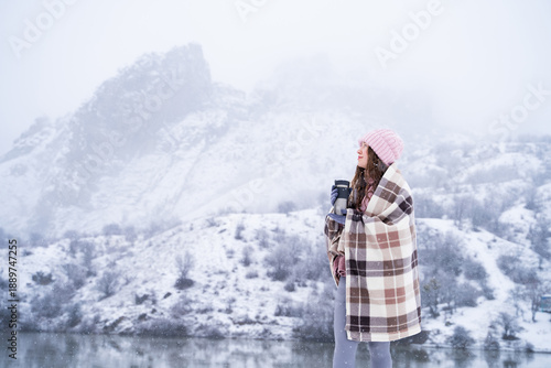 Φωτογραφία Peaceful woman enjoying hot drink from a thermos in winter mountains, wrapped in