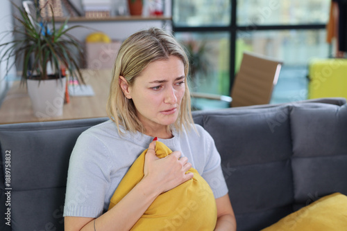 Cuadro en lienzo A young woman sits on a gray couch, holding a bright yellow pillow close to her chest