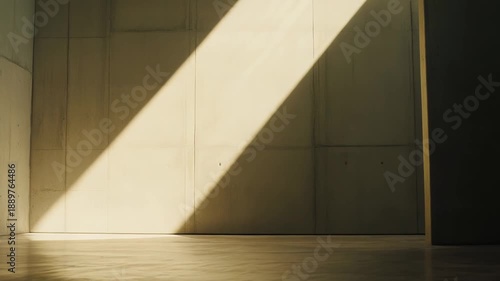 Sunlight diagonally illuminating an empty raw concrete wall and floor inside a minimalist modern architectural space, creating a dynamic contrast of light and shadow