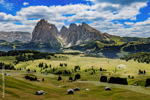 View over the alpine meadows with mountain cabins towards the Langkofel group with the peaks of Langkofel and Plattkofel on the Seiser Alm, Dolomites, South Tyrol, Italy.