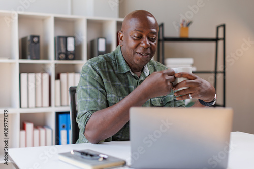 Canvas Print Elderly 60s man on laptop holding a coffee cup, senior looking at laptop screen