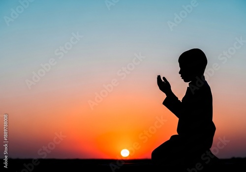 Silhouette of a young boy performing religious prayer (Du'a) during a vibrant sunset or sunrise outdoors.