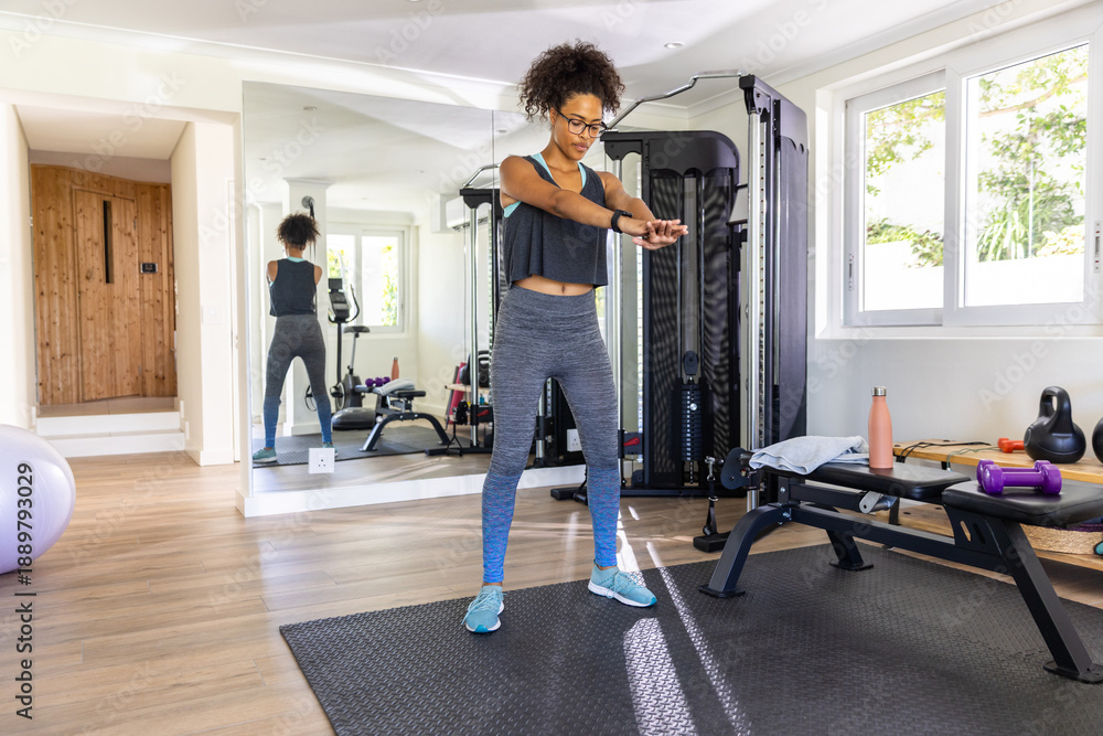 Fototapeta premium African American woman in her 30s holding cable machine handles standing on mat at home gym