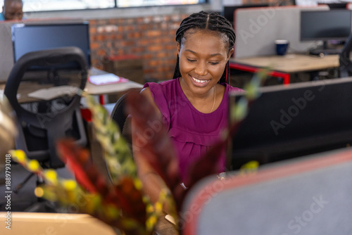 African american woman wearing magenta top, smiling, typing on keyboard at office with monitor