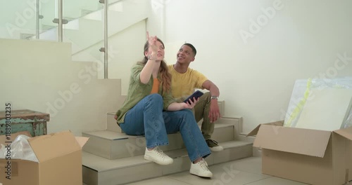 Diverse couple tapping smartphone, unpacking boxes while moving in, dancing then walking in entry