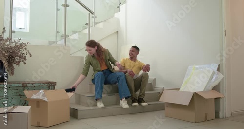 Couple sitting on steps at home laughing at phone, opening box, celebrating move and embracing