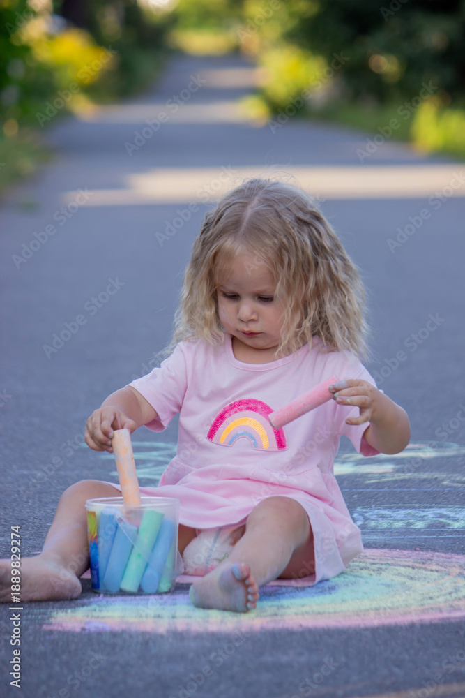 Fototapeta premium Cute little girl drawing a colorful rainbow with chalk on the asphalt road