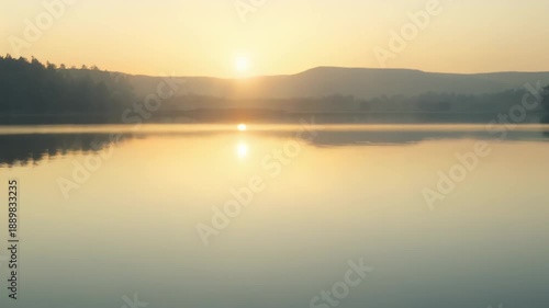 Wallpaper Mural Water surface creating small ripples reflects the warm golden light of the sun rising over blurred hills, creating a tranquil and peaceful natural background for concepts of calm and new beginnings Torontodigital.ca